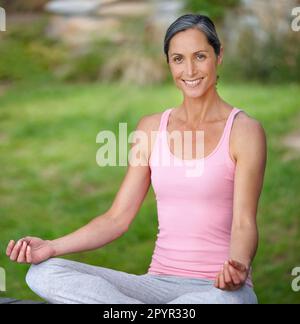 Meditation - Teil ihres Alltags. Eine attraktive reife Frau, die Yoga in Lotusposition praktiziert. Stockfoto