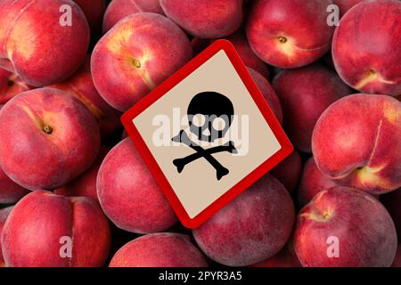 Schädelknochen-Schild auf reifen Pfirsichen, Draufsicht. Vorsicht - giftig Stockfoto