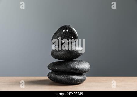 Steine mit gezeichnetem fröhlichem Gesicht auf dem Tisch vor grauem Hintergrund. Zen-Konzept Stockfoto