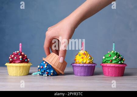 Eine Frau, die einen heruntergefallenen Cupcake am weißen Holztisch abholte, Nahaufnahme. Probleme passieren Stockfoto