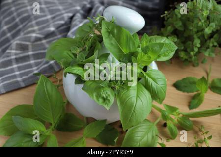 Mörtel mit verschiedenen frischen Kräutern und schwarzen Pfefferkörnern auf Holztisch, Nahaufnahme Stockfoto