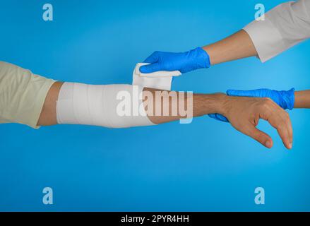 Arzt, der medizinische Verband auf die Hand des Patienten auf hellblauem Hintergrund aufbringt, Nahaufnahme Stockfoto