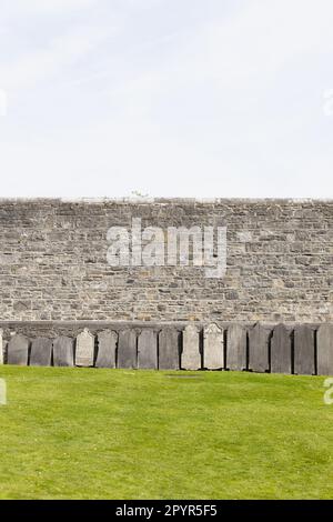 Eine Reihe alter Grabmarkierungen vor einer Steinmauer auf dem Arbour Hill Cemetery in Dublin, Irland. Stockfoto