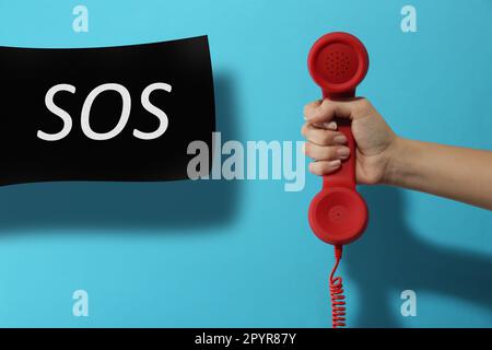 Frau, die das Telefon auf hellblauem Hintergrund hält, Nahaufnahme. Notruf Stockfoto