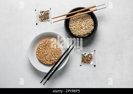 Rohe Instantnudeln in Schüsseln mit Stäbchen und Gewürzen auf weißem Grunge-Hintergrund Stockfoto
