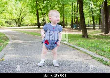 Süßes, weißes Baby, das an einem Sommertag die ersten Schritte im Park macht. Gehen eines Kleinkindes Stockfoto