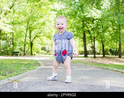 Ein Kleinkind macht die ersten Schritte im Park. Ihr Baby lernt laufen. Babyentwicklung 1-jähriges Mädchen Stockfoto