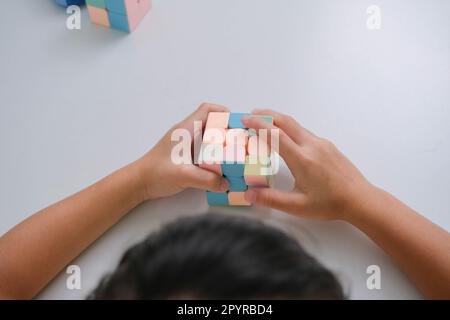 Asiatisches, süßes Mädchen, das Rubiks Würfel in der Hand hält und damit spielt. Rubiks Würfel ist ein Spiel, das die Intelligenz von Kindern erhöht. Bildungswesen Stockfoto