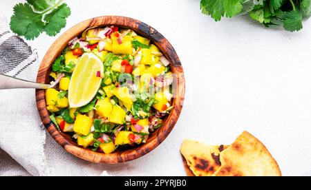 Mango Salsa – scharfe Sauce mit Chili-Paprika, Zwiebeln, Knoblauch, Limette und Koriander in einer Holzschüssel auf weißem Tischhintergrund, Draufsicht Stockfoto