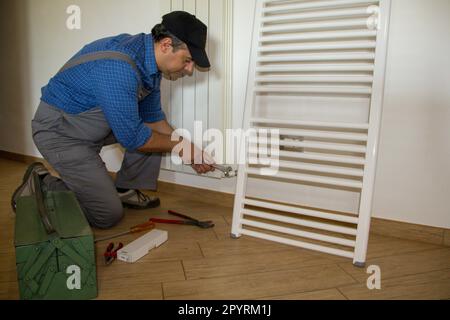 Bild eines Klempners in einem Haus, der Heizkörper mit einem Schraubenschlüssel anbringt. Installation einer Heizung für ein Haus. Stockfoto