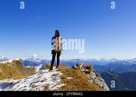 Rückblick auf eine Wanderin auf dem Berggipfel, die die AIPs unter dem blauen, sonnigen Himmel beobachten kann Stockfoto