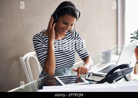 Multitasking zu Hause. Eine junge Geschäftsfrau, die ein Headset trägt, während sie ein digitales Tablet benutzt. Stockfoto