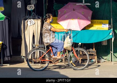 SAMUT PRAKAN, THAILAND, FEBRUAR 07 2023, Eine Frau fährt auf einem Fahrrad auf dem Marktplatz neben einem Stand Stockfoto