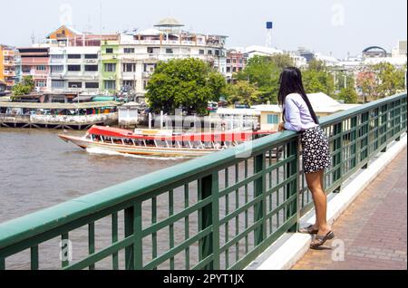 Eine junge Frau schaut von der Brücke über den Fluss Chao Phraya im Zentrum von Bangkok, Thailand Stockfoto