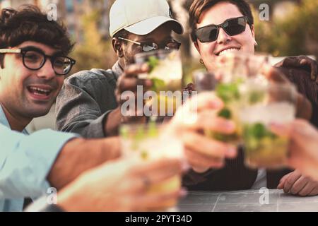 Eine nicht binäre Person mit Sonnenbrille und Nasenpiercing genießt mit ihren multiethnischen Freunden frische Cocktails an einer Bar im Freien. Stockfoto