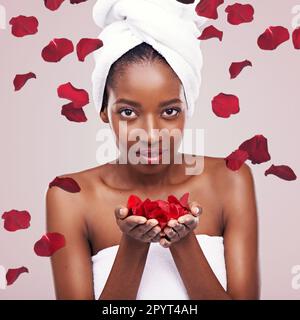 Meine Haut, alles, was sich in Rosen verwandelt. Studiofoto einer schönen jungen Frau in einem Handtuch, umgeben von fallenden Blütenblättern. Stockfoto