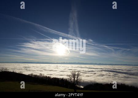 Ein malerischer Blick auf die Sonne hinter Wolken über einem grünen Hügel in der Schweiz Stockfoto