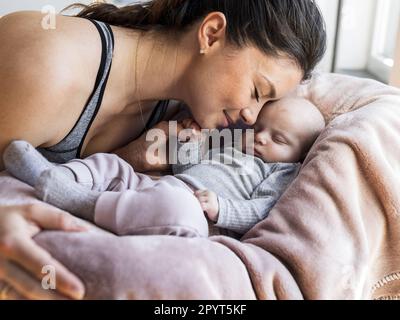 Mama kuschelt mit einem Neugeborenen, das schläft und den Finger der mutter mit einer kleinen Hand hält. Mutterschaftsliebe und Pflegekonzept Stockfoto