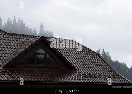 Haus mit neuem braunen Metallziegeldach und Regenrinne. Metallrinne, Dachrinnen und Abflussrohre außen. Stockfoto