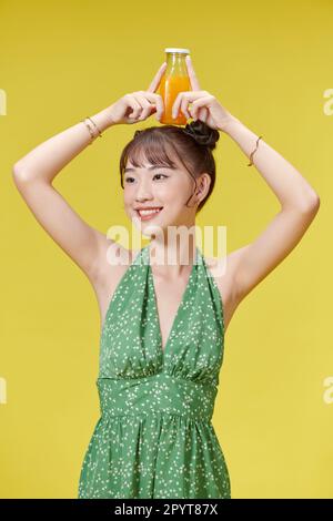 Fröhliches Lächeln, junge asiatische Frau, die frischen Orangensaft in einer Glasflasche trinkt Stockfoto