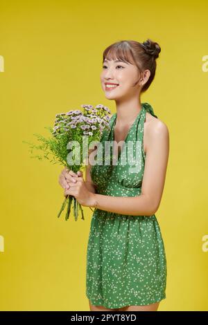 Bild einer jungen asiatischen Frau mit Blumen auf gelbem Hintergrund Stockfoto