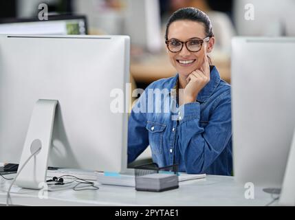 Kommen wir zur Sache. Lächelnde Geschäftsfrau, die an ihrem Schreibtisch sitzt und in die Kamera schaut. Stockfoto
