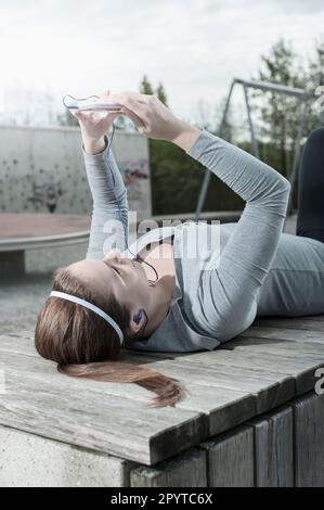 Junge Frau, die nach sportlichem Training eine Pause macht und Sporttestergebnisse auf dem Handy überprüft, Bayern Stockfoto