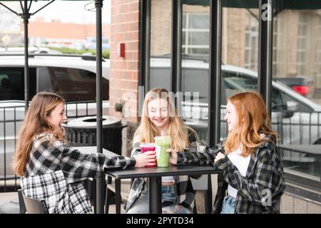 Drei glückliche Teenager-Mädchen, die vor einem Café was trinken. Stockfoto