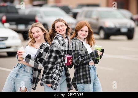 Drei glückliche Teenager-Mädchen, die Drinks auf einem Parkplatz halten. Stockfoto