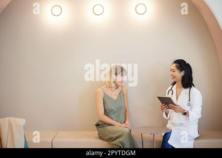 Lächelnde Arztin, die mit einer im Krankenhaus sitzenden Kollegin spricht Stockfoto