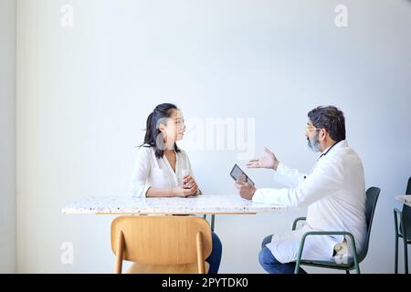 Männlicher Arzt erklärt Patientin auf Stuhl im Krankenhaus Stockfoto