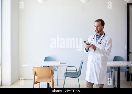 Männlicher Arzt mit Smartphone im Stehen in der Klinik Stockfoto