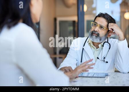 Reifer Arzt hört weiblichen Patienten in der Klinik zu Stockfoto