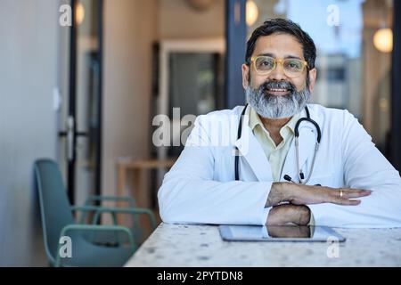 Portrait eines lächelnden männlichen Gesundheitsarbeiters, der am Schreibtisch in der Klinik sitzt Stockfoto