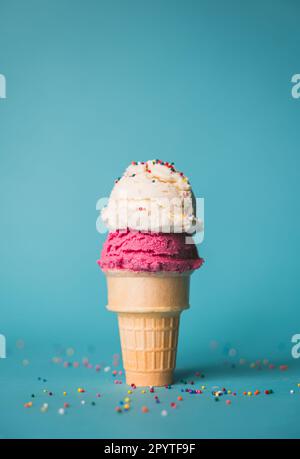 Eiskegel mit zwei Kugeln und Streuseln auf blauem Hintergrund. Stockfoto