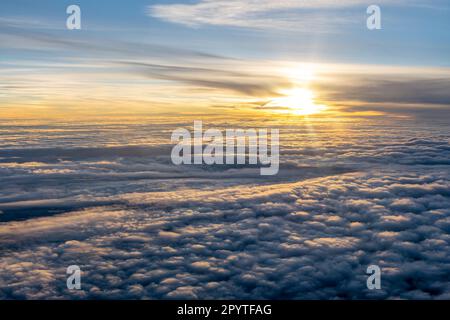 Sonne über einem Wolkenmeer bei Sonnenuntergang durch das Flugzeugfenster zu sehen Stockfoto