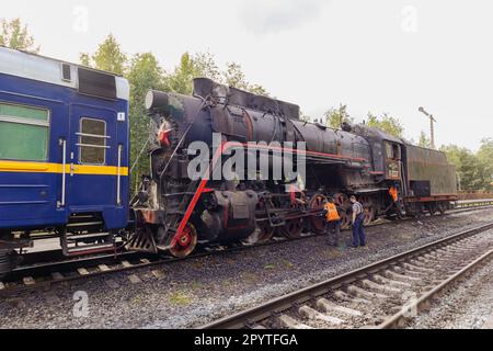 Die Arbeiter schmieren die Räder einer Dampflokomotive im Retro-Look. Ruskeala, Karelien, Russland - 2. September 2022. Stockfoto