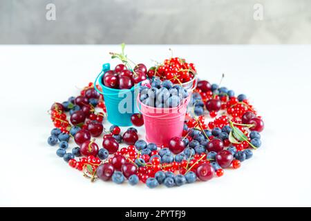 Mischen Sie frische Beeren in kleinen Eimern. Saftige Sommertapete. Weißer Hintergrund. Stockfoto