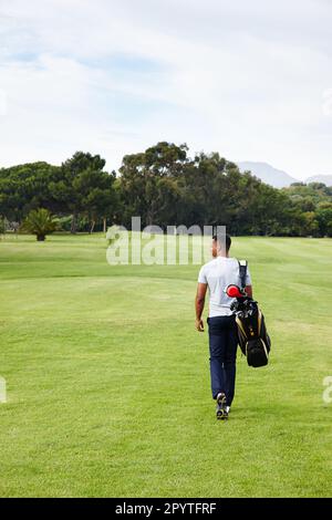Dein einziger Gegner ist, wer du mal warst. Rückansicht eines jungen Mannes, der mit einer Golftasche auf einem Golfplatz läuft. Stockfoto