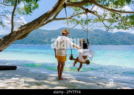 Ein Paar spielt an einer Seilschaukel am Strand von Ko Ra WI Island Süd-Thailand, ein tropischer weißer Sandstrand mit türkisfarbenem Ozean im Tarutao National Park, Koh Rawi, Tambon Ko Tarutao Stockfoto