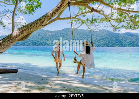 Ein Paar spielt an einer Seilschaukel am Strand von Ko Ra WI Island Süd-Thailand, ein tropischer weißer Sandstrand mit türkisfarbenem Ozean im Tarutao National Park, Koh Rawi, Tambon Ko Tarutao Stockfoto