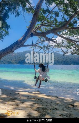 Frauen auf einer Schaukel am Strand der Insel Ko Ra WI im Süden Thailands, tropischer weißer Sandstrand mit türkisfarbenem Ozean im Tarutao Nationalpark, Koh Rawi, Tambon Ko Tarutao Stockfoto
