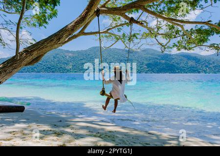 Frauen auf einer Schaukel am Strand der Insel Ko Ra WI im Süden Thailands, tropischer weißer Sandstrand mit türkisfarbenem Ozean im Tarutao Nationalpark, Koh Rawi, Tambon Ko Tarutao Stockfoto