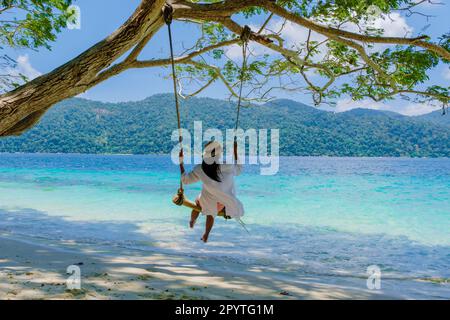 Frauen auf einer Schaukel am Strand der Insel Ko Ra WI im Süden Thailands, tropischer weißer Sandstrand mit türkisfarbenem Ozean im Tarutao Nationalpark, Koh Rawi, Tambon Ko Tarutao Stockfoto