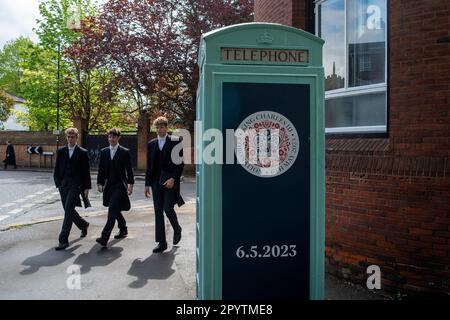 Eton, Windsor, Berkshire, Großbritannien. 5. Mai 2023. Die Jungs vom Eton College gehen an einem Krönungswappen vorbei, an einer Telefonzelle, die den Anlass der Krönung des Königs markiert. Der Sohn von König Charles III., Prinz William und Prinz Harry, ging zur Schule an der berühmten Eton College Public School in Eton, Windsor. Kredit: Maureen McLean/Alamy Live News Stockfoto