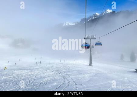 AUS DER SERIE ADELBODEN Seilbahn im Schnee vor der winterlichen Landschaft in Adelboden, Berner Oberland, Kanton Bern, Schweiz. Die malerische Stadt Adelboden ist eine Schweizer Idylle in den Berner Alpen, beeindruckende Gipfel, einzigartige Winterlandschaft, beliebtes Skigebiet, Alpenweiden, Rauschende Wasserfälle, gemütliche Holzhäuser. Aufgrund des Klimawandels und immer weniger Schnee, orientiert sich das klassische Wintersportresort neu, und die Sommersaison gewinnt an Bedeutung Stockfoto