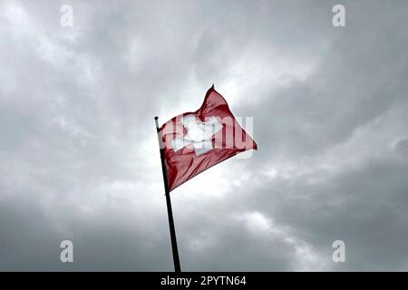 AUS DER SERIE ADELBODEN Flag der Schweiz vor einer winterlichen Landschaft rund um die Tschentenalp in Adelboden, Berner Oberland, Kanton Bern, Schweiz. Die malerische Stadt Adelboden ist eine Schweizer Idylle in den Berner Alpen, beeindruckende Gipfel, einzigartige Winterlandschaft, beliebtes Skigebiet, Alpenweiden, Rauschende Wasserfälle, gemütliche Holzhäuser. Aufgrund des Klimawandels und immer weniger Schnee, orientiert sich das klassische Wintersportresort neu, und die Sommersaison gewinnt an Bedeutung. Stockfoto