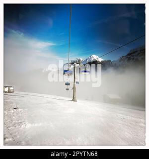 AUS DER SERIE ADELBODEN Seilbahn im Schnee vor der winterlichen Landschaft in Adelboden, Berner Oberland, Kanton Bern, Schweiz. Die malerische Stadt Adelboden ist eine Schweizer Idylle in den Berner Alpen, beeindruckende Gipfel, einzigartige Winterlandschaft, beliebtes Skigebiet, Alpenweiden, Rauschende Wasserfälle, gemütliche Holzhäuser. Aufgrund des Klimawandels und immer weniger Schnee, orientiert sich das klassische Wintersportresort neu, und die Sommersaison gewinnt an Bedeutung. Foto mit iPhone, Hipstamatic App. Stockfoto