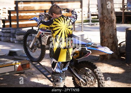 Ich bereite seine Fahrt vor. Rückansicht eines Motocross-Fahrers, der sein Motorrad von einem Anhänger nimmt. Stockfoto