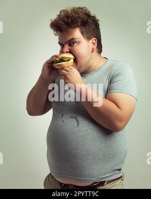 Komm nicht in die Nähe meines Burgers. Studiofoto eines übergewichtigen Mannes, der in einen Burger beißt. Stockfoto